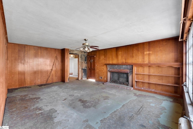 unfurnished living room featuring wooden walls, ceiling fan, a fireplace, and unfinished concrete flooring