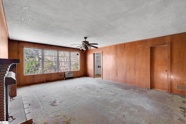 unfurnished living room with a textured ceiling, ceiling fan, wooden walls, a fireplace, and visible vents