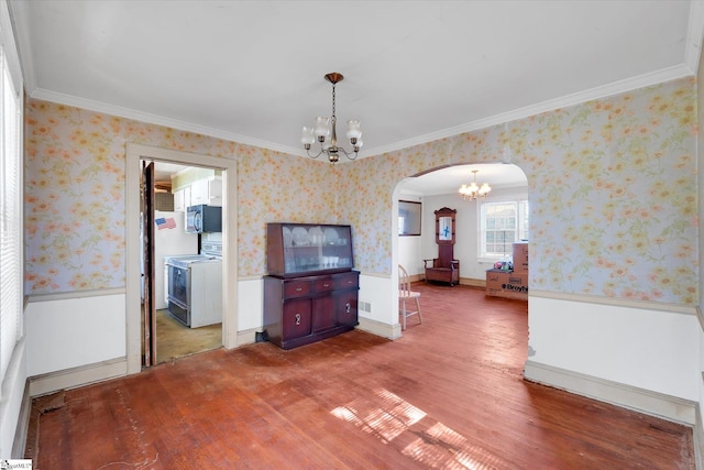 unfurnished dining area with wallpapered walls, arched walkways, a wainscoted wall, and an inviting chandelier