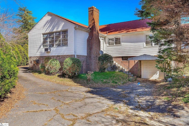 view of property exterior featuring aphalt driveway, an attached garage, brick siding, stairway, and a chimney