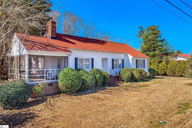 view of front of property featuring a sunroom, a chimney, and a front yard