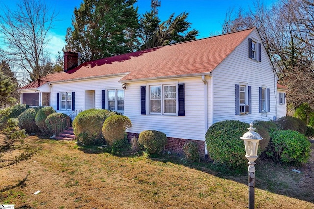 cape cod home featuring a shingled roof, a chimney, an attached garage, cooling unit, and a front yard