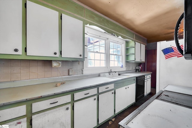 kitchen featuring a sink, black dishwasher, light countertops, backsplash, and freestanding refrigerator