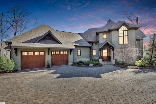 view of front facade with a shingled roof, decorative driveway, stone siding, and an attached garage