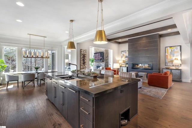 kitchen with a large fireplace, dark wood-type flooring, a sink, beamed ceiling, and dark countertops