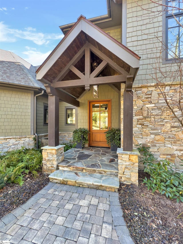 entrance to property featuring covered porch, stone siding, and a shingled roof