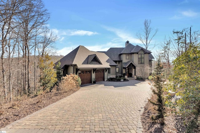 french provincial home with a garage, decorative driveway, and a chimney