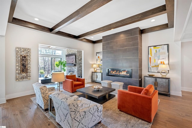 living area with wood-type flooring, a fireplace, beamed ceiling, and baseboards