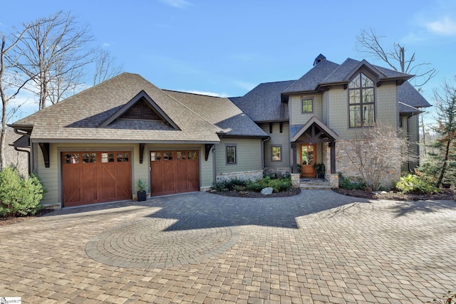 view of front of home featuring a garage, stone siding, decorative driveway, and roof with shingles