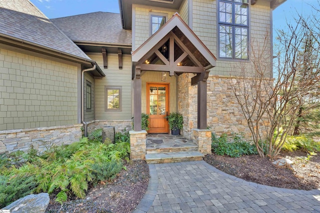 view of exterior entry featuring a shingled roof and stone siding