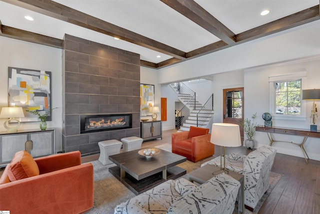 living area with baseboards, a tile fireplace, hardwood / wood-style floors, stairs, and beam ceiling