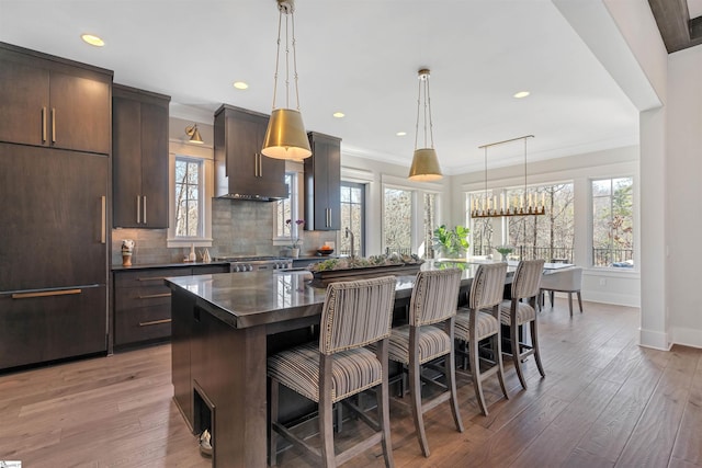 kitchen with a center island, a kitchen bar, paneled fridge, and exhaust hood