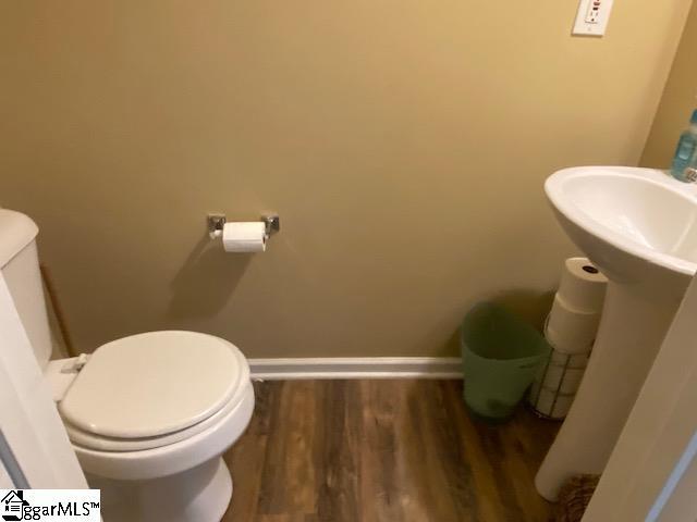 half bath with baseboards, a sink, toilet, and wood finished floors