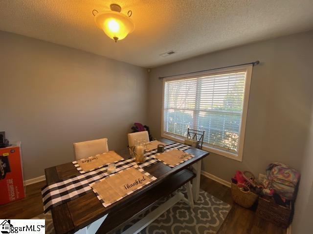 dining area with baseboards, a textured ceiling, visible vents, and wood finished floors