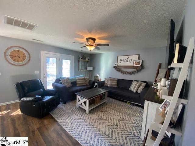 living area featuring a textured ceiling, wood finished floors, visible vents, and a ceiling fan