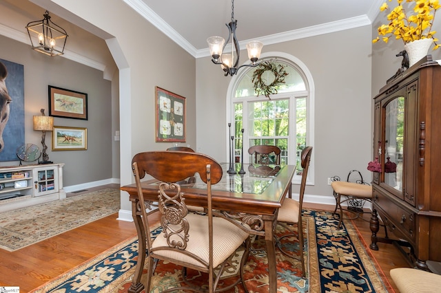 dining space with baseboards, ornamental molding, a notable chandelier, and wood finished floors