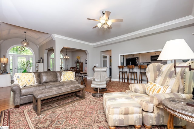 living room featuring baseboards, arched walkways, ornamental molding, wood finished floors, and ceiling fan with notable chandelier