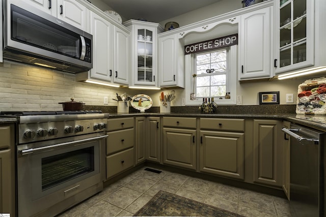 kitchen with tasteful backsplash, appliances with stainless steel finishes, glass insert cabinets, white cabinetry, and dark stone counters