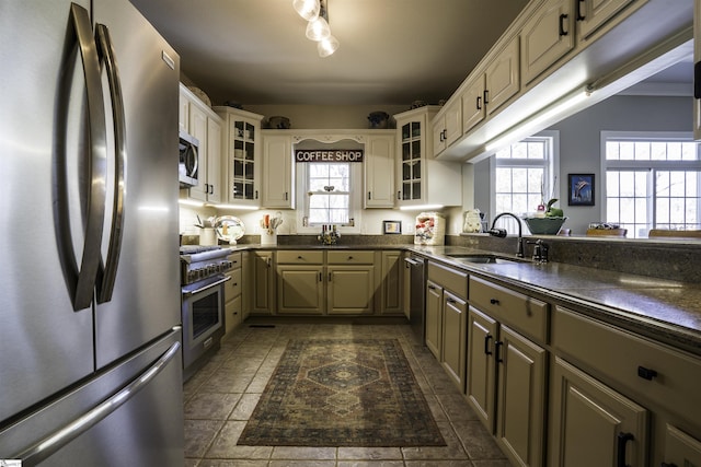 kitchen featuring appliances with stainless steel finishes, dark countertops, a sink, and glass insert cabinets