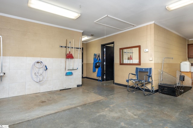 interior space featuring concrete flooring, ornamental molding, attic access, and concrete block wall