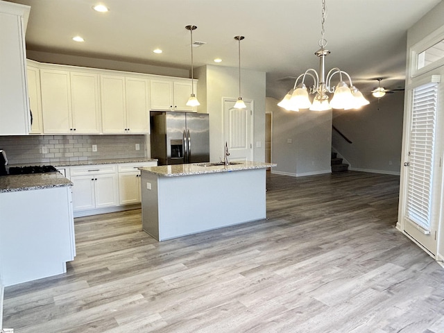 kitchen with decorative backsplash, a kitchen island with sink, a sink, light wood-type flooring, and stainless steel fridge