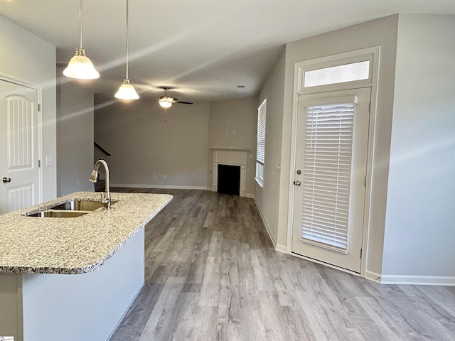 kitchen featuring light stone counters, pendant lighting, a fireplace, a sink, and wood finished floors