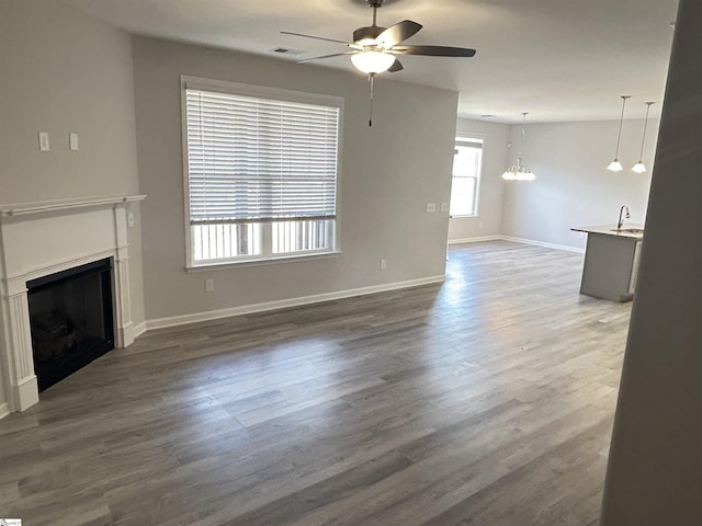 unfurnished living room with a fireplace, visible vents, dark wood finished floors, and ceiling fan with notable chandelier