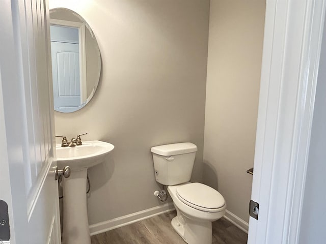 bathroom featuring toilet, a sink, baseboards, and wood finished floors