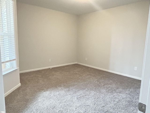 unfurnished room with baseboards and dark colored carpet