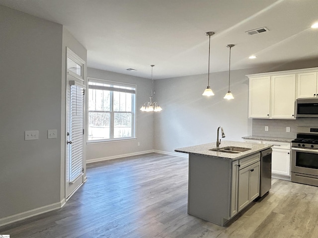 kitchen featuring light wood-style flooring, stainless steel appliances, a sink, decorative backsplash, and light stone countertops