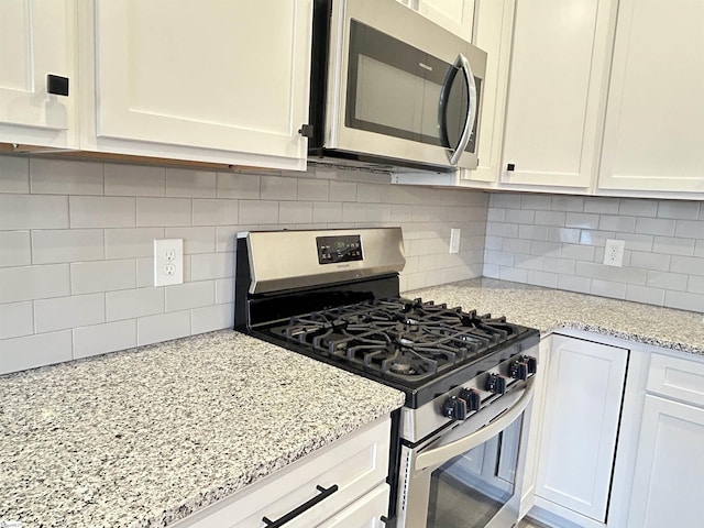 kitchen with stainless steel appliances, white cabinets, decorative backsplash, and light stone countertops