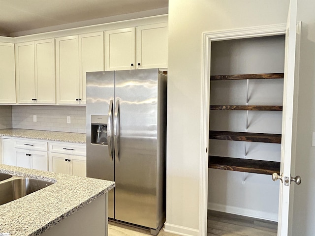 kitchen featuring light stone counters, stainless steel fridge, decorative backsplash, and white cabinetry