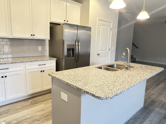 kitchen with stainless steel refrigerator with ice dispenser, hanging light fixtures, backsplash, light wood-style floors, and a sink