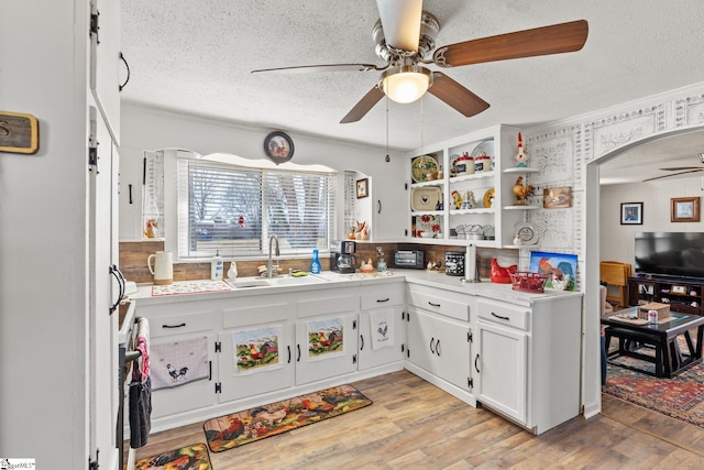 kitchen with light wood-type flooring, a textured ceiling, arched walkways, and a sink