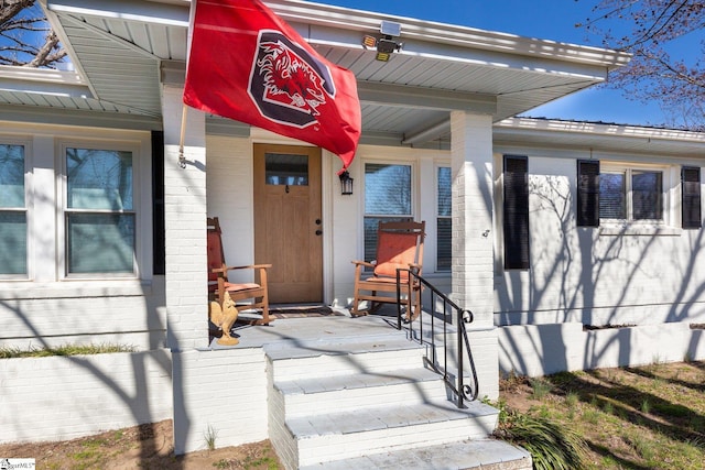 entrance to property featuring covered porch, brick siding, and crawl space