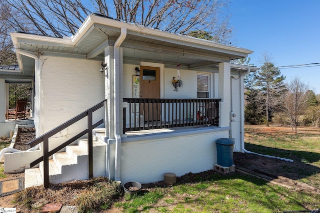 entrance to property featuring a porch and brick siding