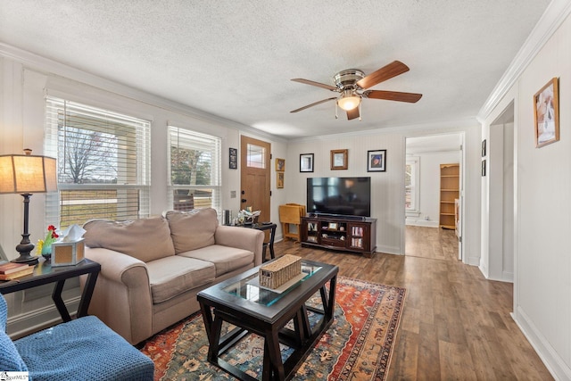 living area featuring ceiling fan, a textured ceiling, ornamental molding, and wood finished floors