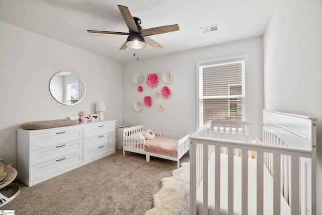 bedroom with a crib, multiple windows, visible vents, and light colored carpet