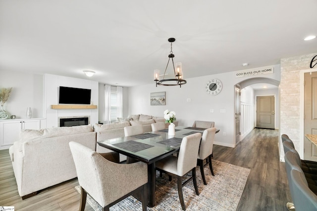 dining space featuring baseboards, arched walkways, wood finished floors, and a glass covered fireplace