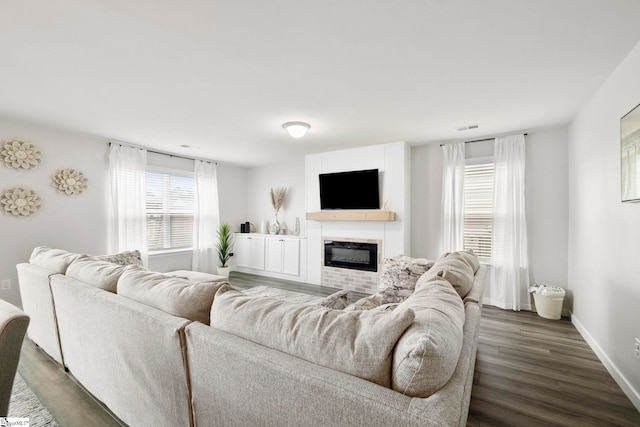 living area with wood finished floors, a glass covered fireplace, visible vents, and baseboards