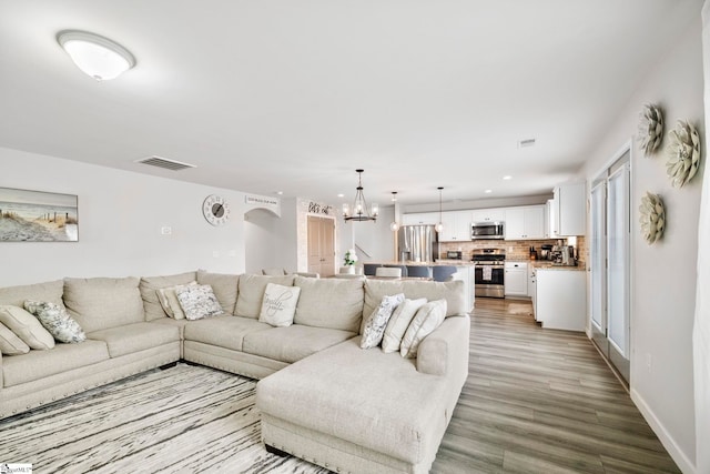 living area with visible vents, a notable chandelier, light wood-style flooring, and baseboards