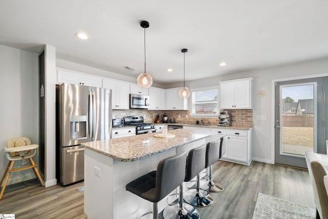 kitchen with white cabinets, light stone counters, stainless steel appliances, light wood-type flooring, and backsplash