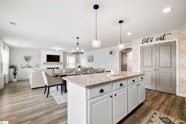 kitchen featuring arched walkways, a fireplace, wood finished floors, visible vents, and a center island