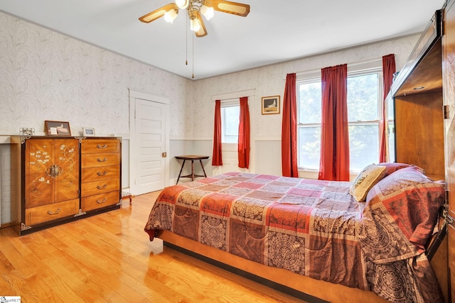 bedroom with a ceiling fan, wood finished floors, a wainscoted wall, and wallpapered walls