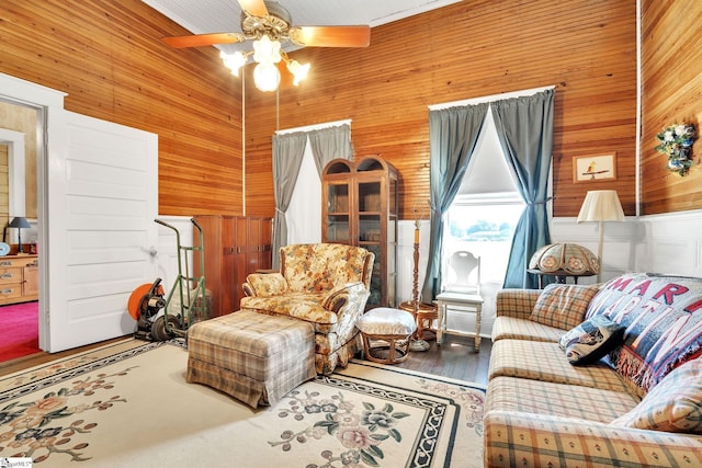 living area with a ceiling fan, wooden walls, a towering ceiling, and wood finished floors