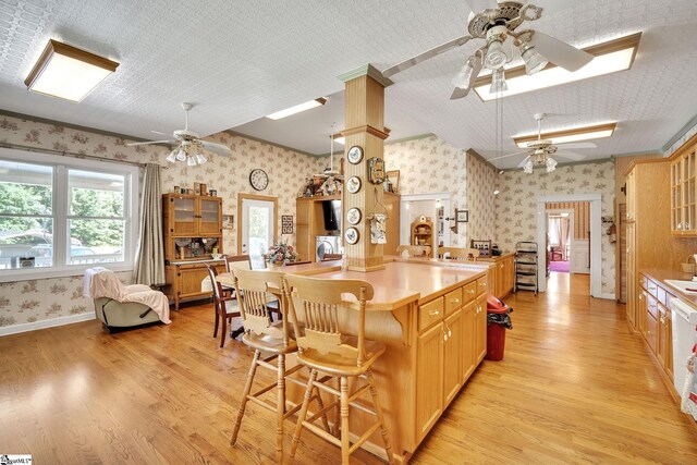 kitchen featuring wallpapered walls, light wood finished floors, baseboards, a ceiling fan, and a breakfast bar area