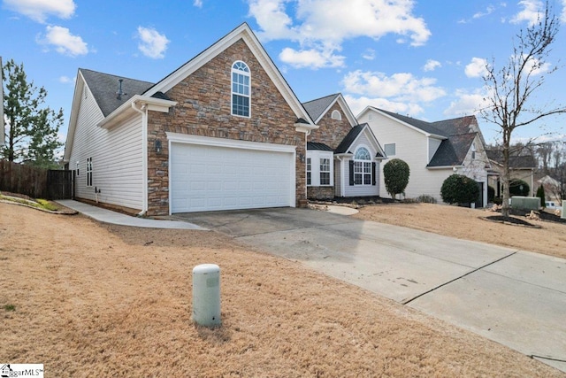 traditional-style home with stone siding, driveway, an attached garage, and fence