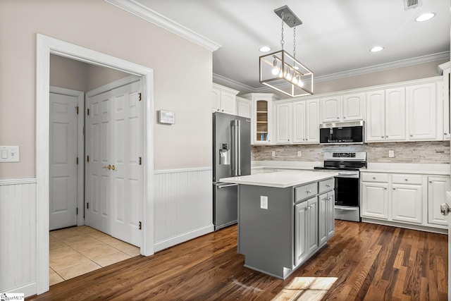 kitchen with stainless steel appliances, a wainscoted wall, ornamental molding, and white cabinetry