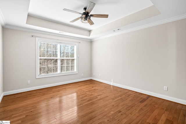 spare room with light wood-style floors, baseboards, and a raised ceiling