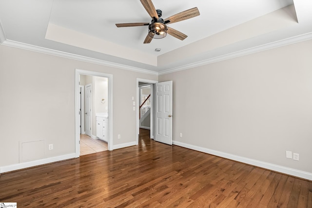 unfurnished bedroom featuring connected bathroom, wood finished floors, baseboards, a tray ceiling, and crown molding